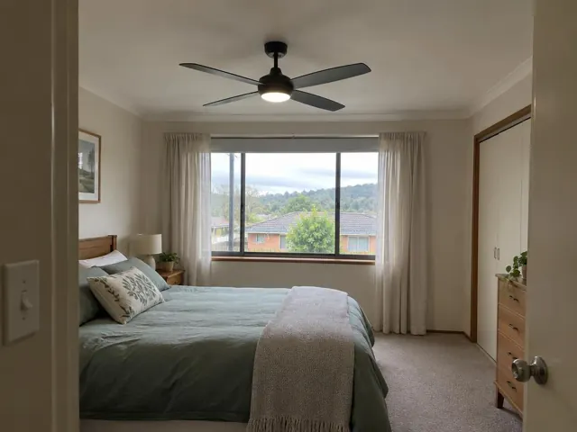 Bedroom with a black ceiling fan, bed, window and curtains in a carpeted home in Glendale