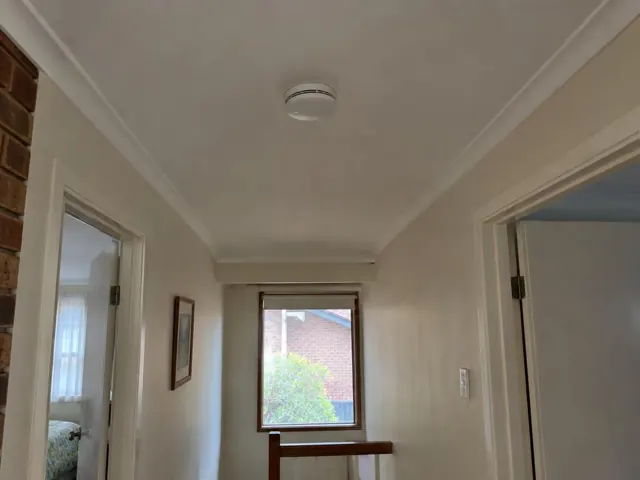 Ceiling smoke alarm in a beige hallway with doors and a window in Cardiff